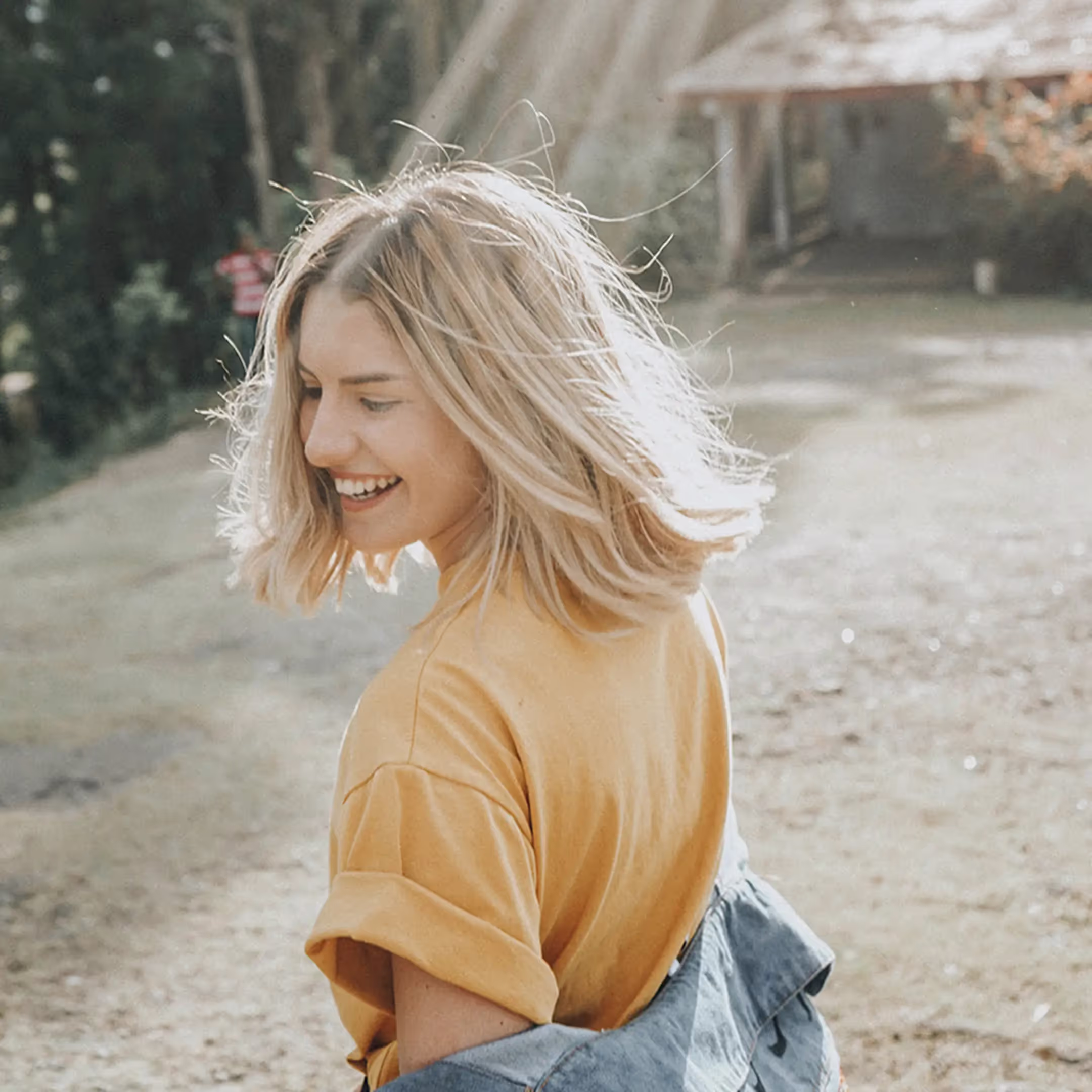 A smiling woman in a yellow shirt and jeans.