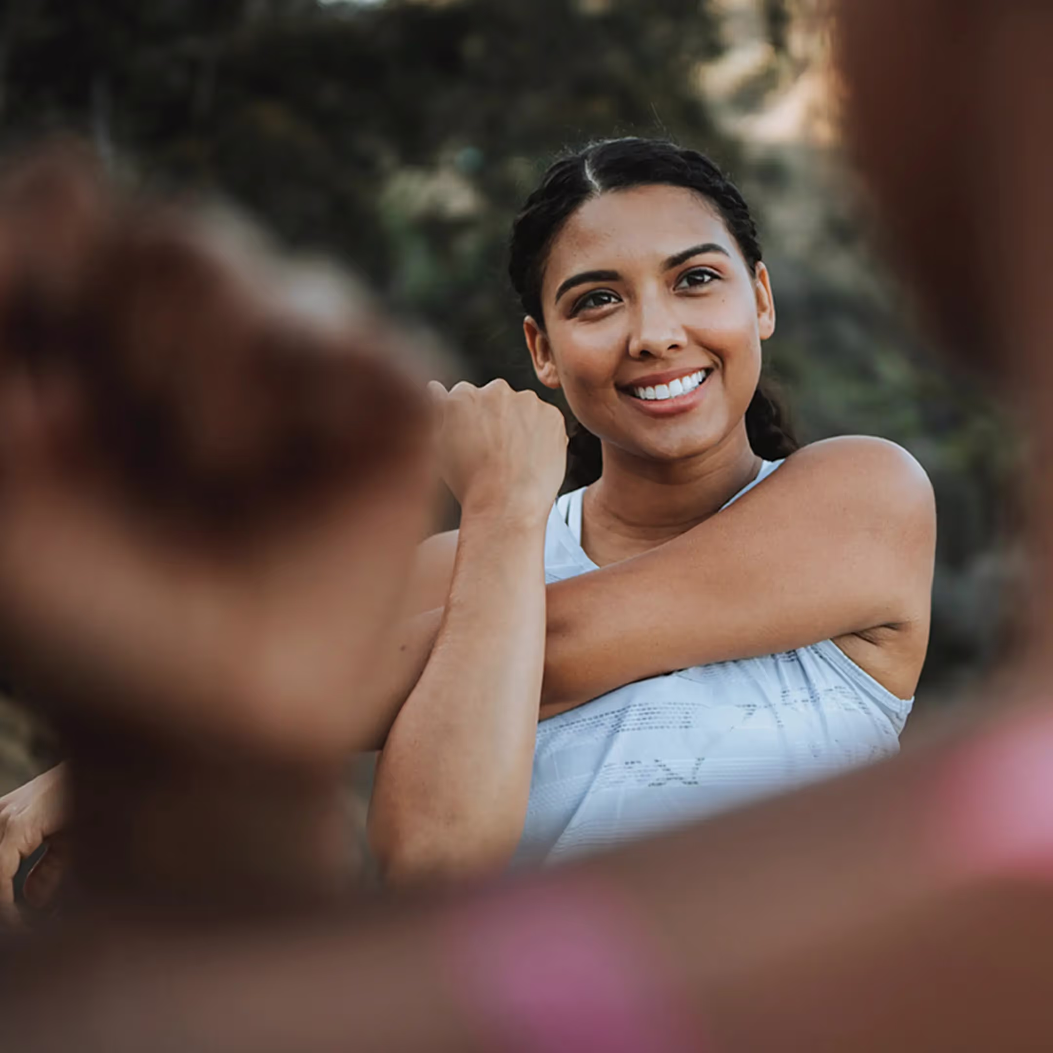 A woman happily holds a stretch, radiating joy with her smile as she prepares to go for a run with a friend.