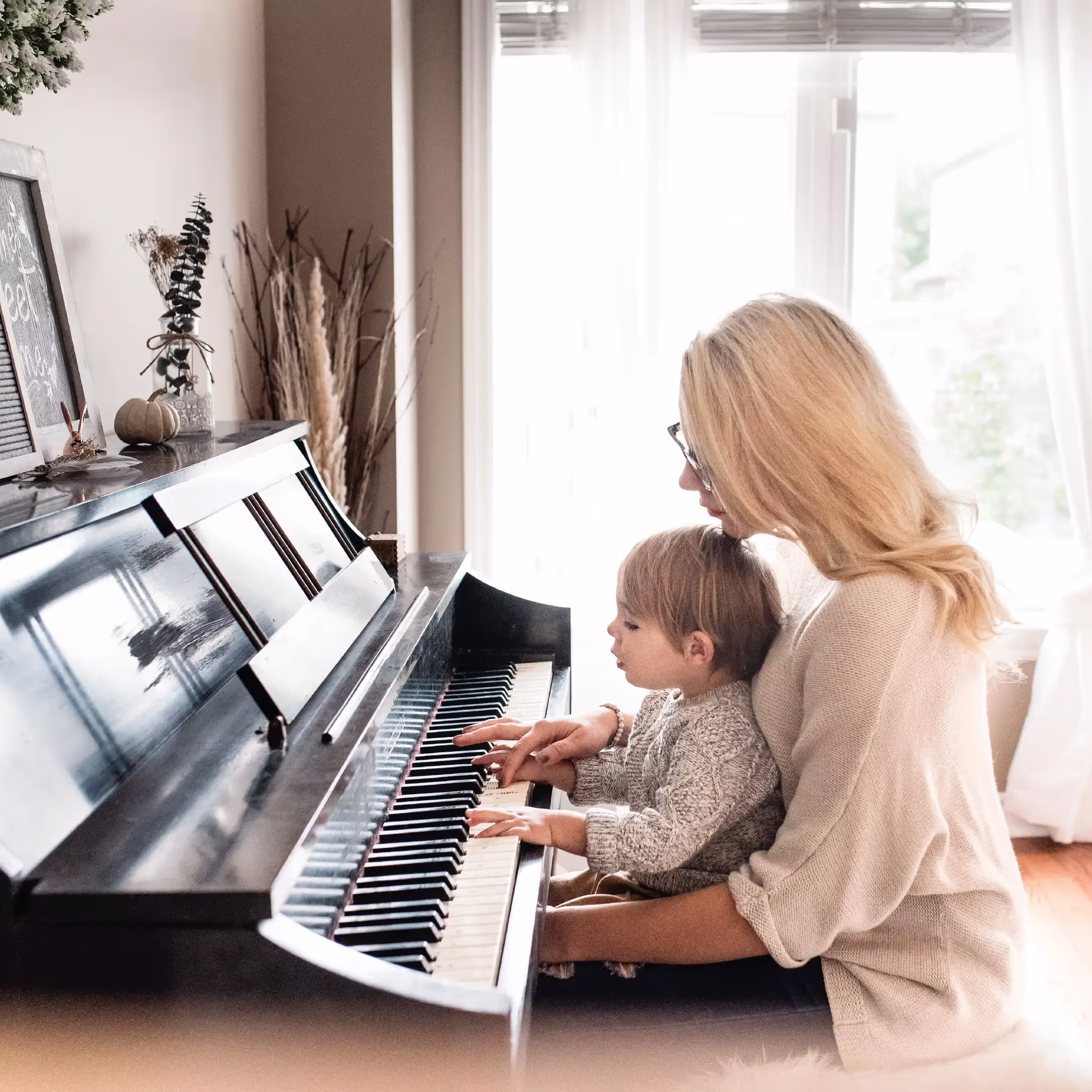 A grandmother sitting at a piano with her granddaughter in her lap as they play the piano together.