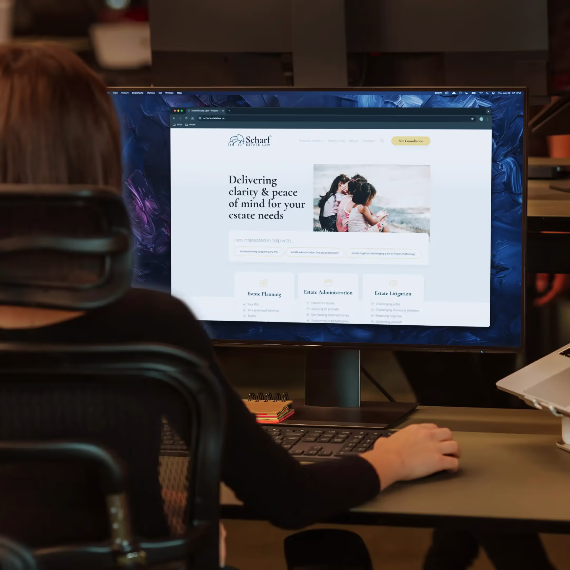 A woman sitting in an office looking at her computer monitor that is displaying the Scharf Estate Law website